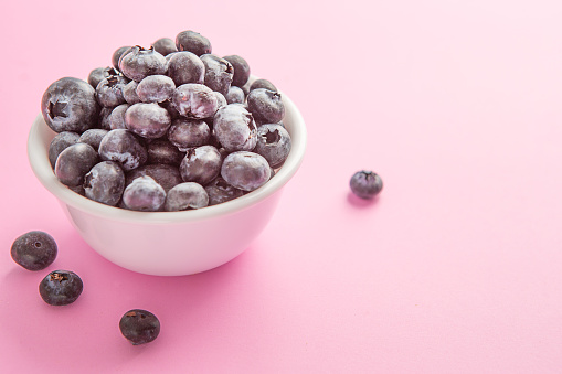 Over flowing white bowl of blueberries on pink background.