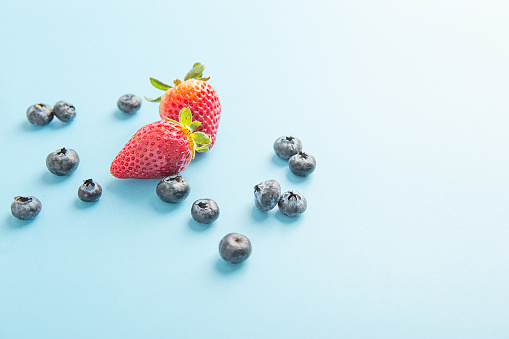 Strawberries and blueberries scattered on blue background.