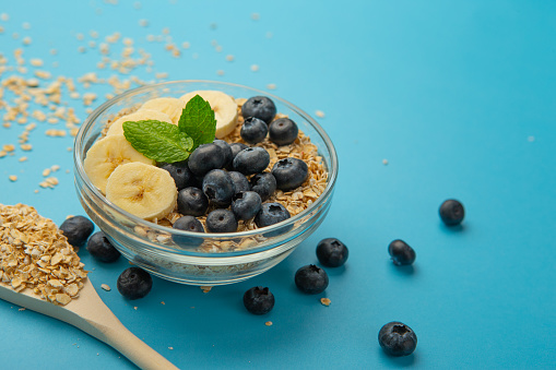 Oatmeal flakes bowl with banana and blue berries on blue background.