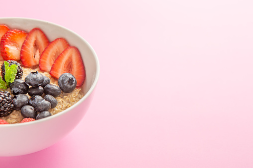 Oatmeal bowl with mixed berries on pink background