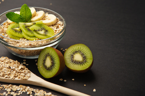 Oatmeal flakes bowl with banana and kiwi topping on dark background.