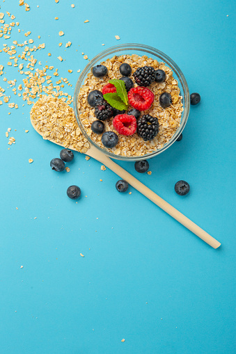 Oatmeal flakes bowl with banana and blue berries on blue background.