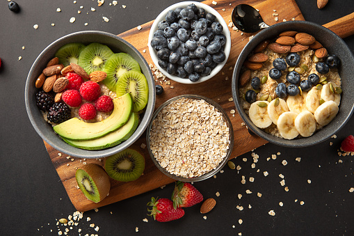 Above view of multiple Healthy Oatmeal bowl with scattering oats flakes on wooden serving tray on grey background.