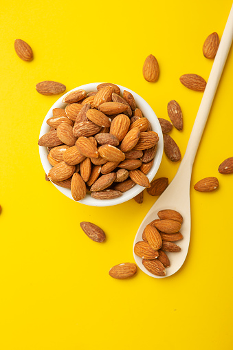Over flowing bowl of roasted almond on yellow background.