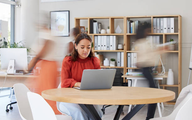 mulher de negócios asiática séria navegando na internet no laptop em escritório ocupado. profissional étnico focado trabalhando enquanto colegas correm em movimento embaçado. empreendedor e designer criativo usando tecnologia - typing busy business women - fotografias e filmes do acervo