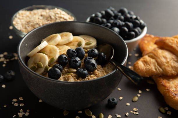 Bowl of oatmeal with mixed fruits topping Healthy Oatmeal bowl with banana and blue berries topping grey background. Oatmeal stock pictures, royalty-free photos & images