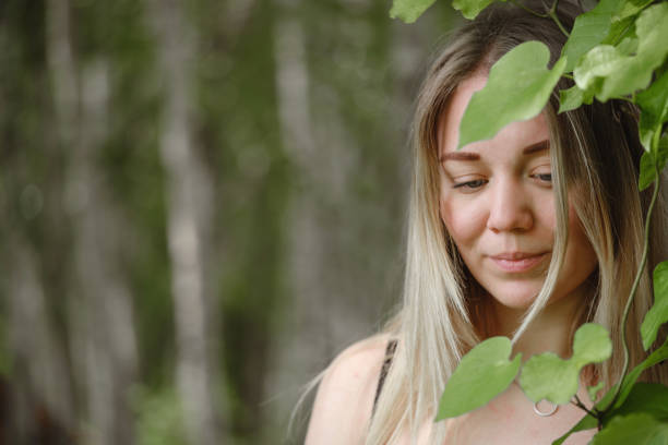 Dreamy woman looking though green leaves over blurred natural background. Banner with copy space. Fresh and beautiful young female, clean skin, ecofriendly environment