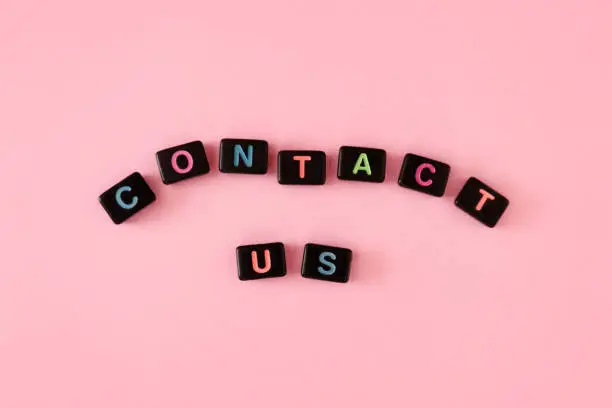 Contact us button concept. Black beads on trendy pink background making word. Support, helpdesk, office communication theme. Connecting with customers and business owners. Phrase made of small letters