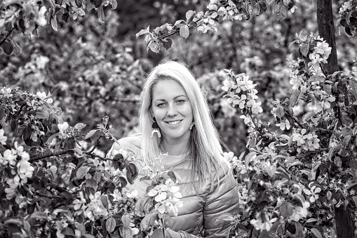 black and white portrait of a smiling blonde woman in a blossoming spring garden, selective focus