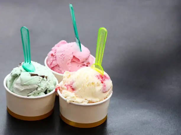 Various colorful ice cream sorts with  in paper cups on black background