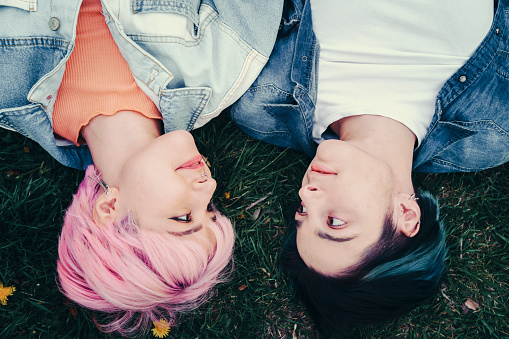 Two young lgbt women are lying down on grass in a park