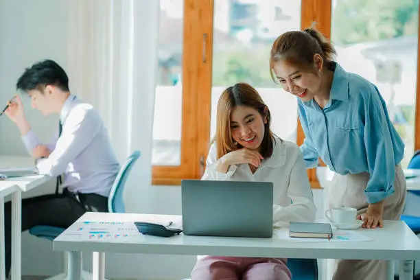 Photo of Asian and Caucasian corporate executives discuss business in a conference room of three young businessmen and women discussing tech startups about product roadmaps, and collaboration ideas.