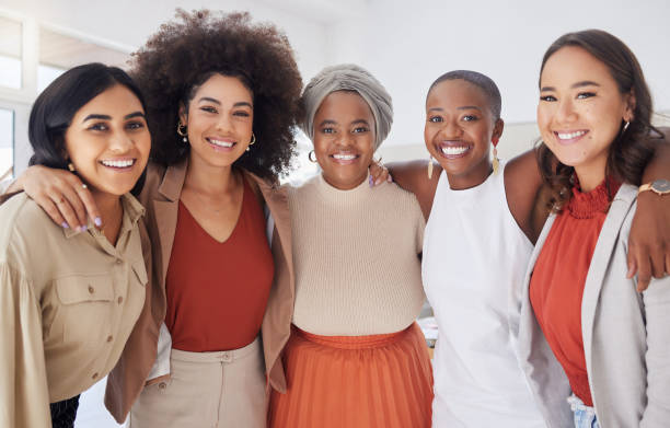 portret zróżnicowanej grupy uśmiechniętych etnicznych kobiet biznesu stojących razem w biurze. ambitny, szczęśliwy, pewny siebie profesjonalny zespół kolegów obejmujący się, a jednocześnie czujący się wspierany i wzmocniony - tylko kobiety zdjęcia i obrazy z banku zdjęć