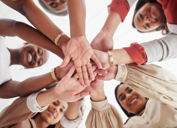 Low angle diverse group of ambitious smiling businesswomen huddled together with hands stacked in middle. Smiling ethnic team of professional colleagues feeling motivated, united, supported and ready Low angle diverse group of ambitious smiling businesswomen huddled together with hands stacked in middle. Smiling ethnic team of professional colleagues feeling motivated, united, supported and ready mid section stock pictures, royalty-free photos & images