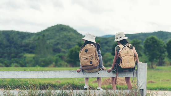 Asian two children traveler sitting on the white fence outdoors adventure, tourism for destination leisure trips with mountain, education explore and relax in nature park. Travel vacations Concept