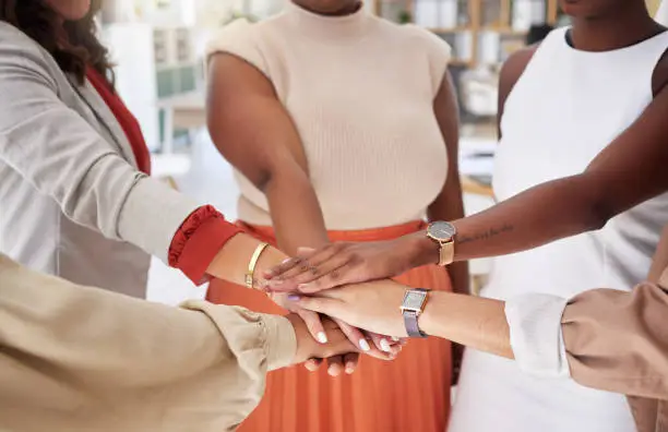 Photo of Diverse group of unknown ambitious businesswomen huddled together with hands stacked in middle. Empowered ethnic team of professional colleagues feeling motivated, united, supported, ready for success