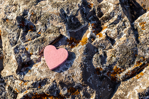 gray stone texture with lichen and heart symbol. red wooden heart on stone