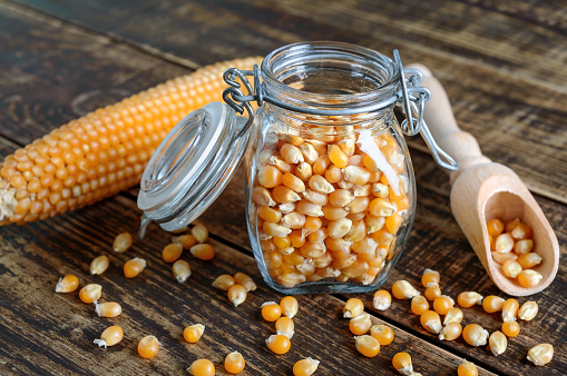 Corn grains in a glass jar on a wooden background. Maize for popcorn