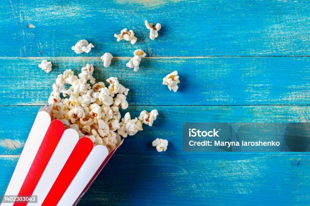 Fresh Popcorn Spilled From A Cardboard Striped Cup On A Blue Wooden Background With Copy Space Top View Stock Photo - Download Image Now