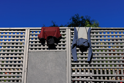 Two wetsuits drying in the sun on a wooden lattice fence.