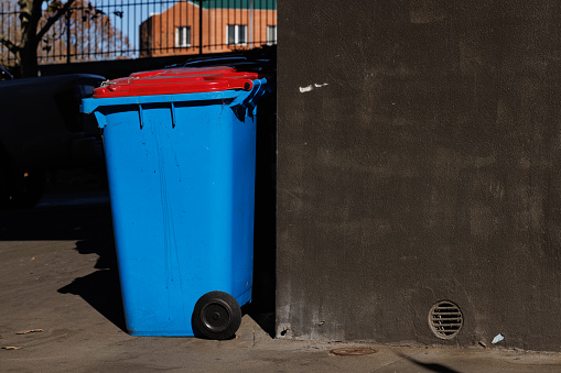 Blue plastic rubbish bin against a building wall in the sun.