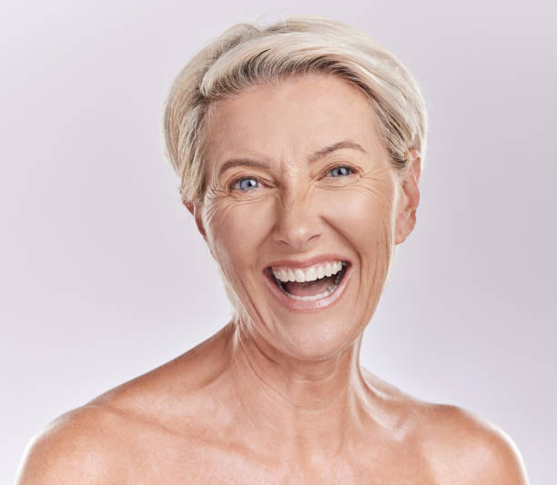 幸せな笑顔の成熟した白人女性の肖像画は、紫色のコピースペースの背景に対してスタジオで彼女の肌の世話をしながら、肯定的で陽気なように見えます。スキンケアルーチンをしている年� - shirtless caucasian freshness relaxation ストックフォトと画像