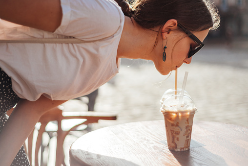 Stylish girl drink cold coffee on the terrace of cafe. Summertime lifestyle portrait of young woman