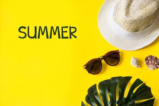 Beach accessories on the yellow background - sunglasses and striped hat. Summer is coming concept.Tropical leaves Monstera. Summer flat lay, top view. Text Summer.