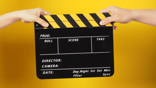 istock Two hands send and hold a Black clapper board or movie slate on yellow background. 1402310918