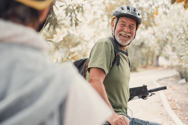 dwoje szczęśliwych starych dojrzałych ludzi cieszących się i jeżdżących razem na rowerach, aby być sprawnym i zdrowym na świeżym powietrzu. aktywni seniorzy bawiący się w przyrodzie. portret pewnego starca uśmiechającego się podczas wyciecz - cycling senior adult sports helmet men zdjęcia i obrazy z banku zdjęć