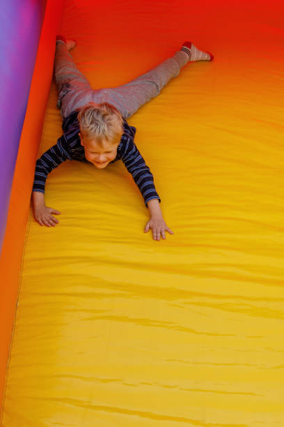 istock Little boy is actively playing on a children's inflatable trampoline. He slides down on his stomach. Bright red-yellow colors. Free copy space. 1402312931
