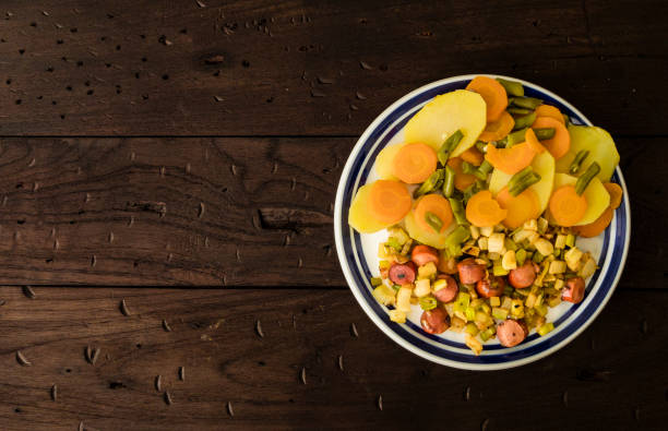 High angle view of cooked potato with green beans and slice of carrots. Also slices of sausage of chicken meat with onions.Delicious dinner at home.As salad slices of ripe avocado with salt.