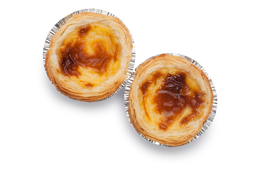 Studio shot of small custard tarts in foil casing cut out against a white background