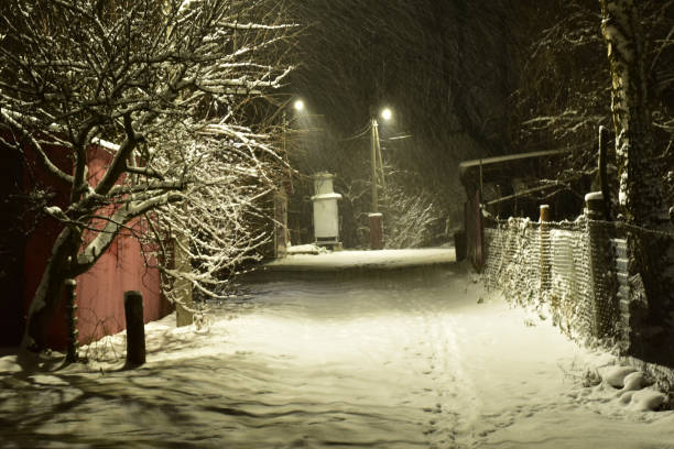 rural road covered with snow illuminated by the lights of lanterns. - january winter icicle snowing imagens e fotografias de stock