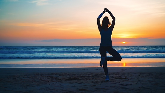 Silhouette Woman practice yoga tree pose to meditation with summer vacation beach happiness and relaxation. Calm female exercise with yoga meditate ocean beach with sunset golden time. Mental health.