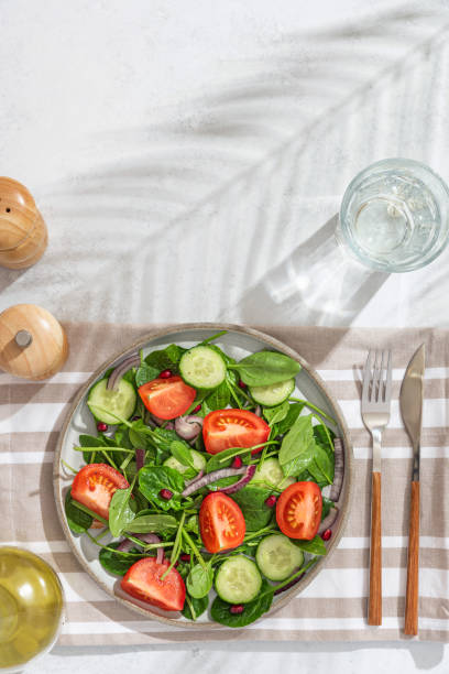 istock Summer vegetable salad with tomatoes, spinach and pomegranate on white table with hard light and palm leaf shadow 1402326502