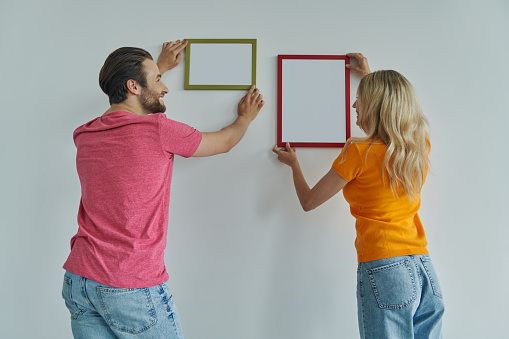 Beautiful young couple hanging picture frames at the wall and smiling