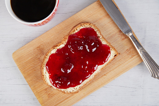 coffee mug, a piece of white bread with strawberry jam and a silver knife, view from above