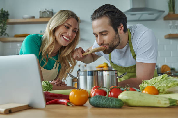 istock Cheerful young couple tasting something from a pan at the domestic kitchen 1402328579
