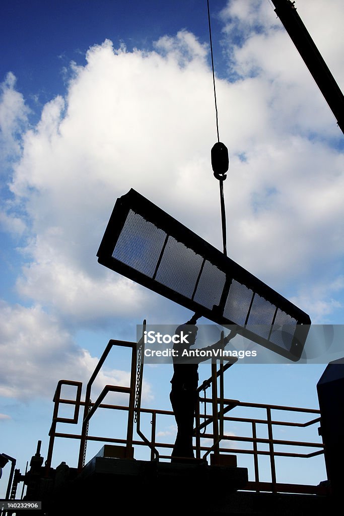 Worker silhouette with crane Worker assists in installing a crane-lifted screen at the seawater intake of a power plant Back Lit Stock Photo