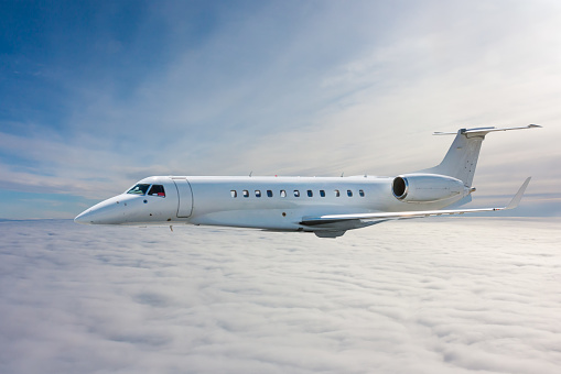 White modern luxury private jet flies in the air above the clouds
