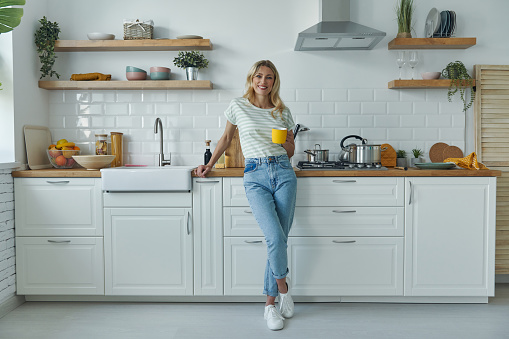 Full length of attractive young woman leaning at the kitchen desk and smiling