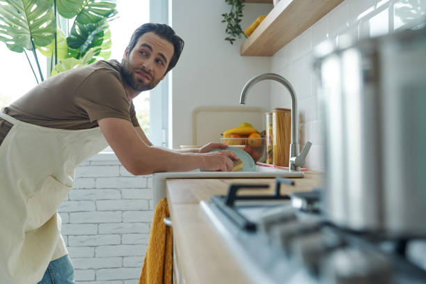 Bored young man washing dishes at the domestic kitchen stock photo
