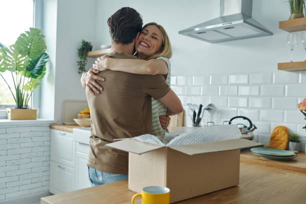 Young couple embracing and smiling while open box laying on the kitchen counter