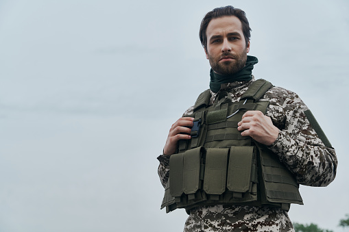 Confident young man in military uniform looking at camera while standing outdoors