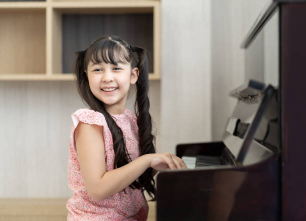 glückliches asiatisches mädchen, das in der schule klavier spielt. lächelnde mädchen üben klavier im wohnzimmer zu hause. bildungs- und kompetenzkonzept. - music learning child pianist stock-fotos und bilder