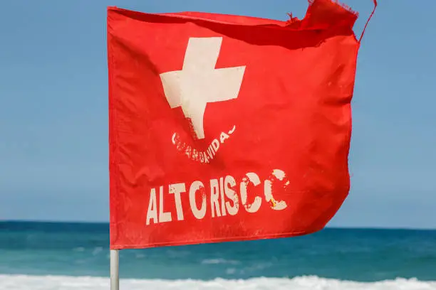 Photo of red current signaling flag, written high risk on a beach in Rio de Janeiro, Brazil.