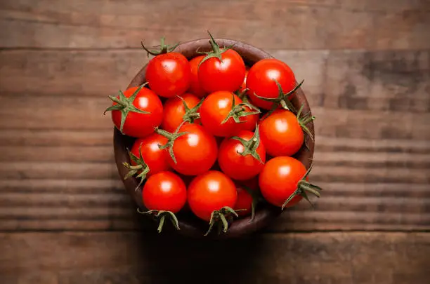 Red cherry tomatoes in a wooden bowl on a wooden background