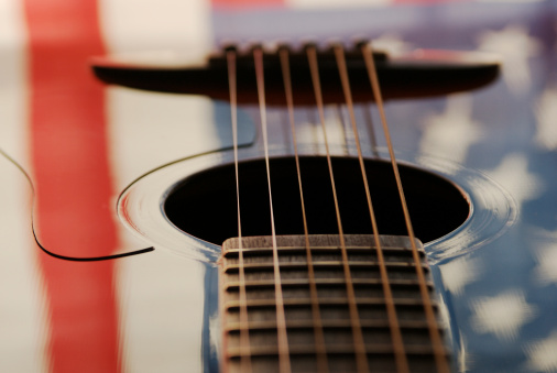 Detail image of guitar with reflection of U.S. Flag on surface, and selective shallow focus on strings.