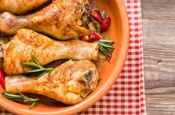 Roasted chicken legs with rosemary, garlic and red chili pepper on rustic wooden background. Top view.